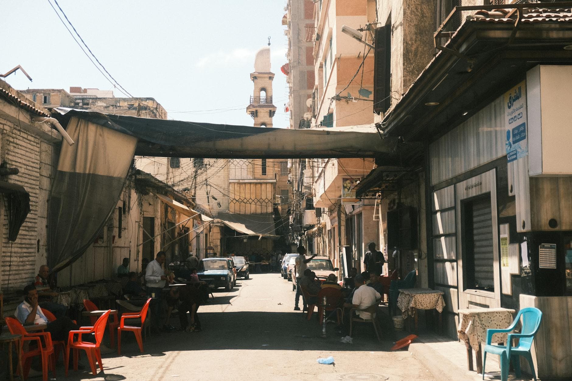Lively street in Alexandria, Egypt with a mosque and locals at coffee houses.