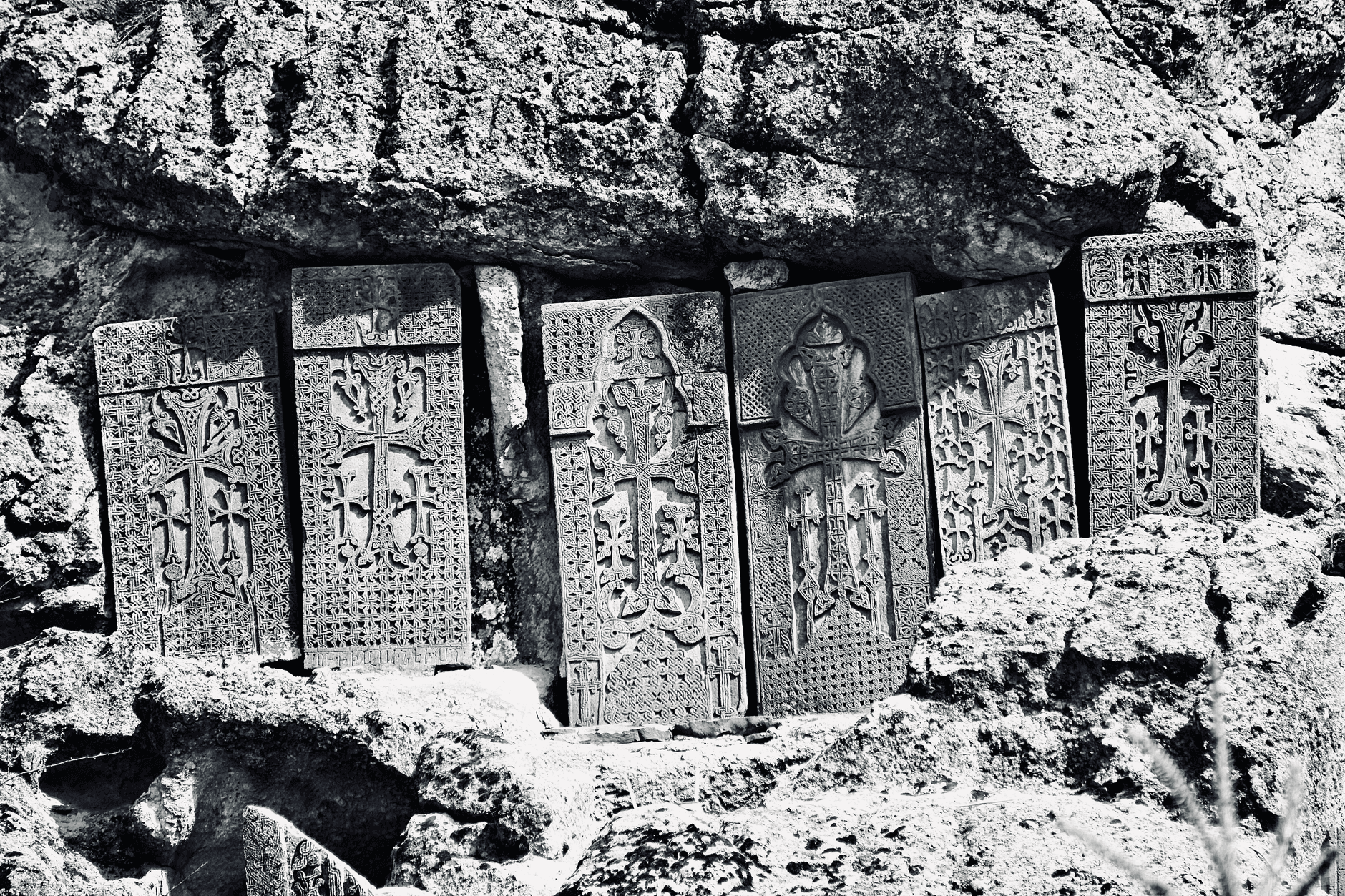 Black and white photo of historic Armenian khachkars carved in stone, sunlit.