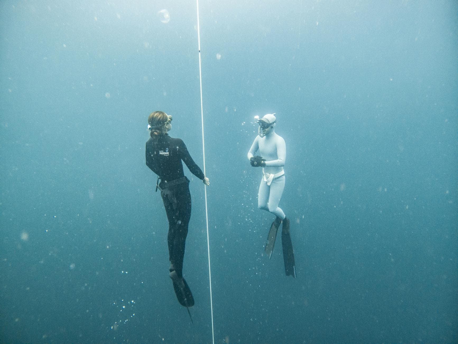Two freedivers explore deep blue waters in Lombok, Indonesia, using guide rope for orientation.