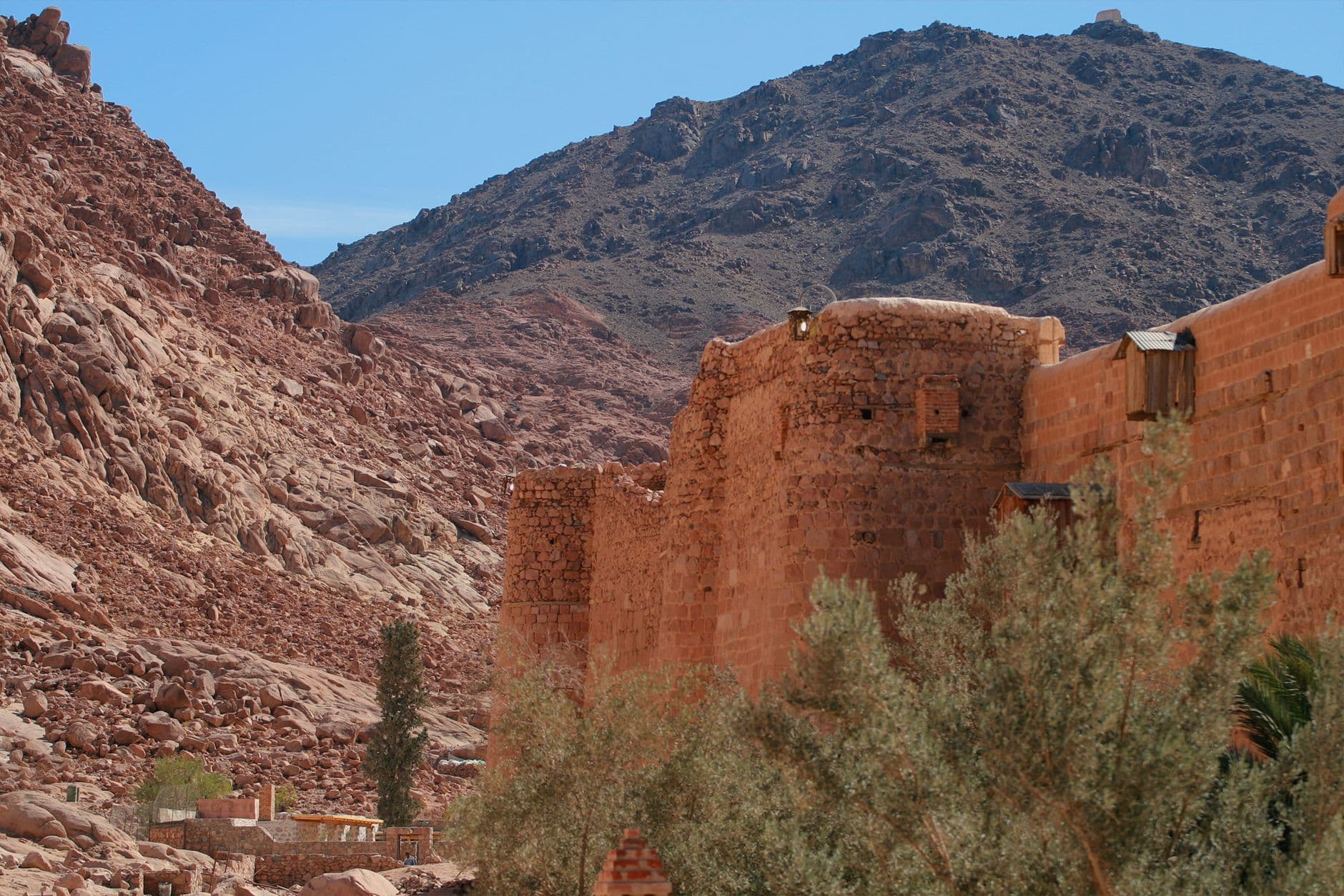Majestic stone monastery wall amidst rugged desert mountains under a clear blue sky.