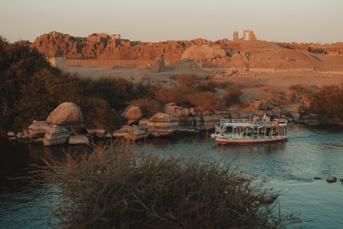 A boat sails on the nile river near ancient ruins.