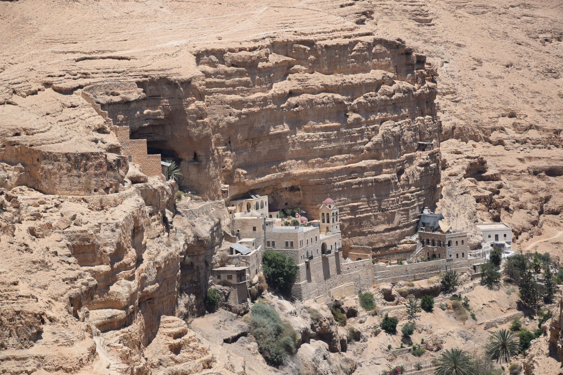 Aerial view of St George's Monastery nestled in the cliffs of Wadi Qelt, illuminated by bright sunlight.