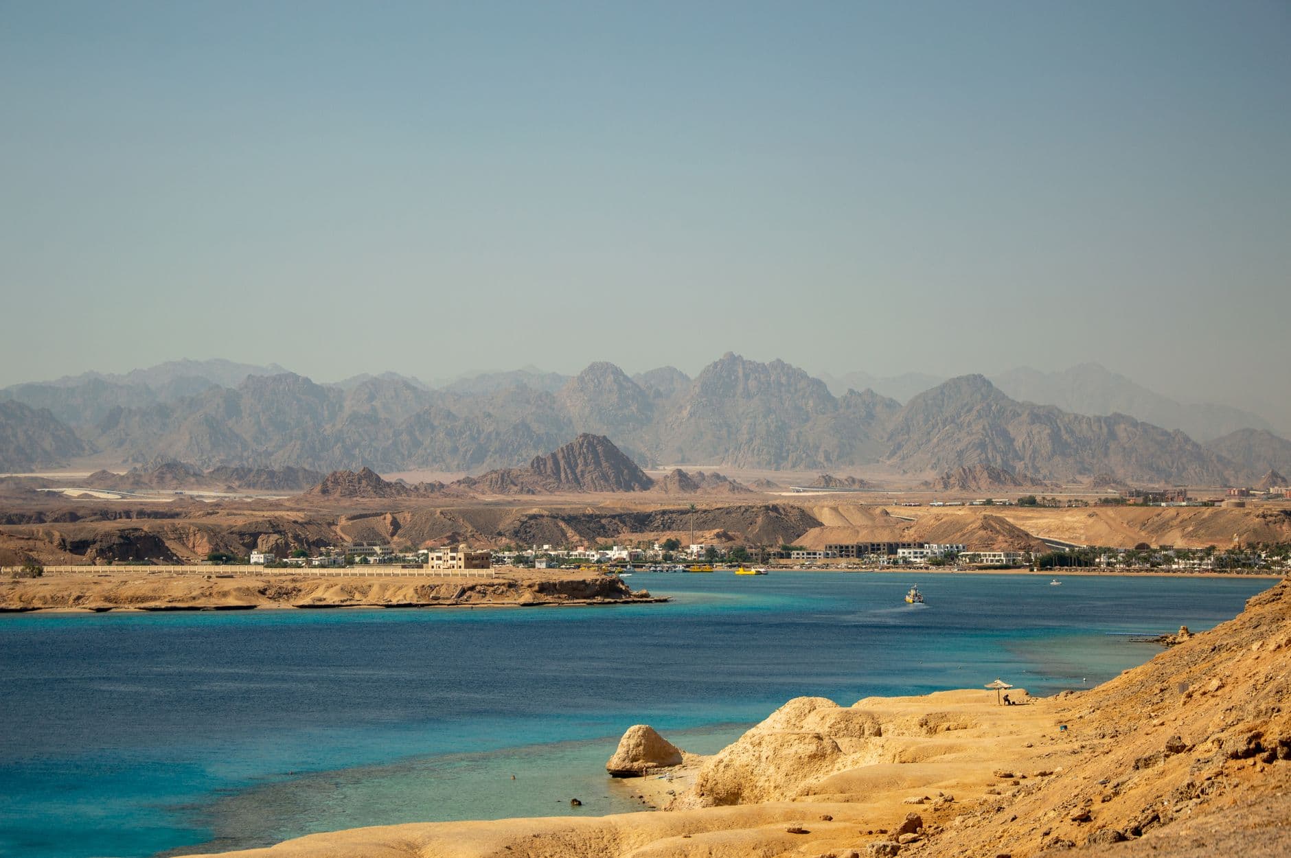 Panoramic view of a coastal town with turquoise waters and rugged mountains in the background.