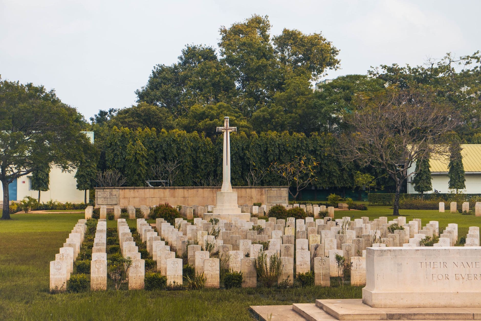 Peaceful military cemetery with rows of tombstones and a central cross monument.