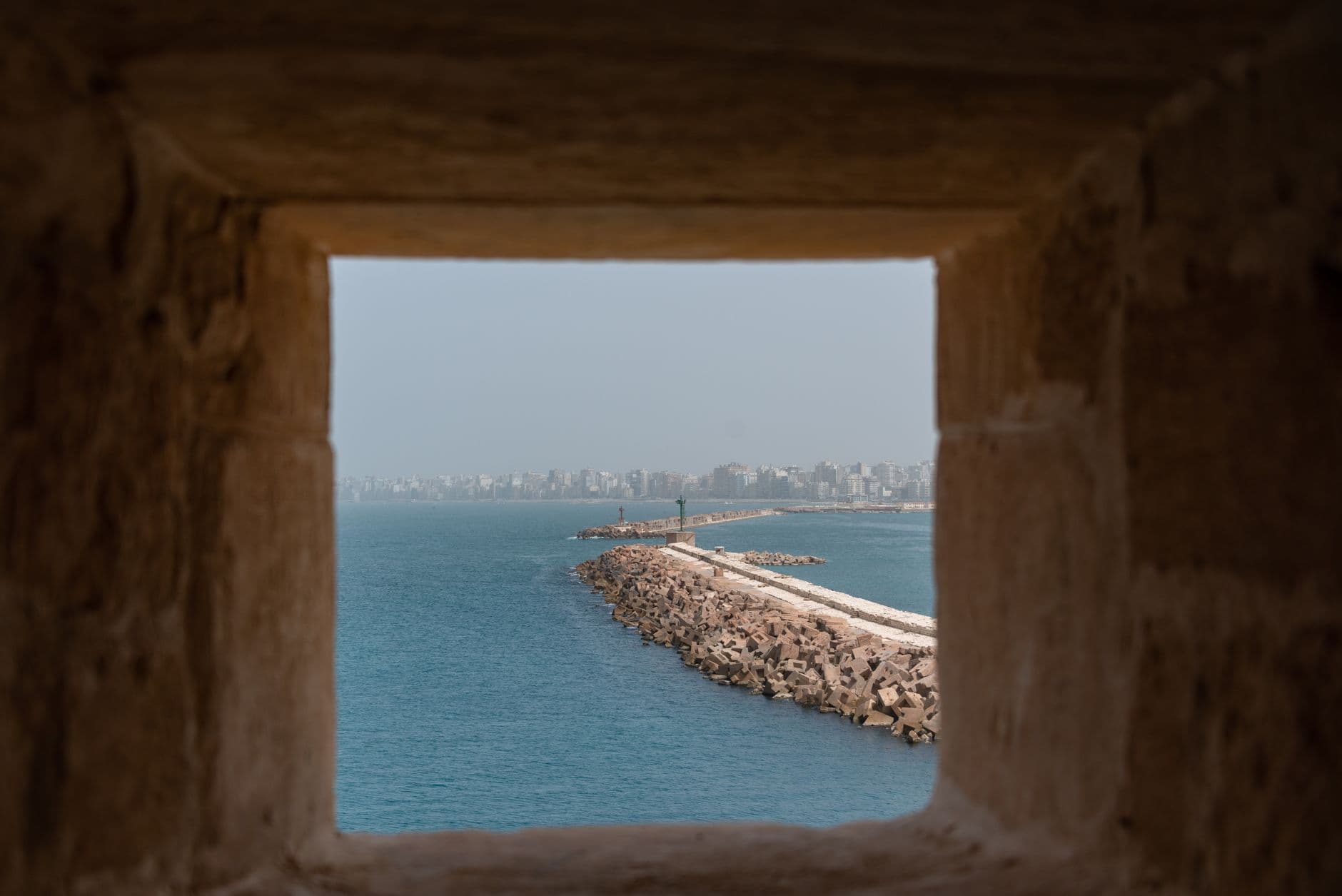 A peaceful harbor view from an ancient fort window with calm sea and distant city skyline.