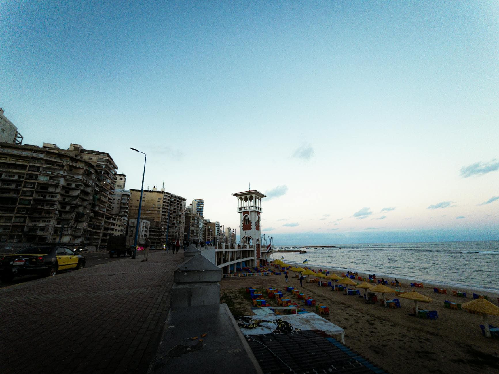 Beautiful sunset over Alexandria beach with vibrant umbrellas and cityscape views in Egypt.