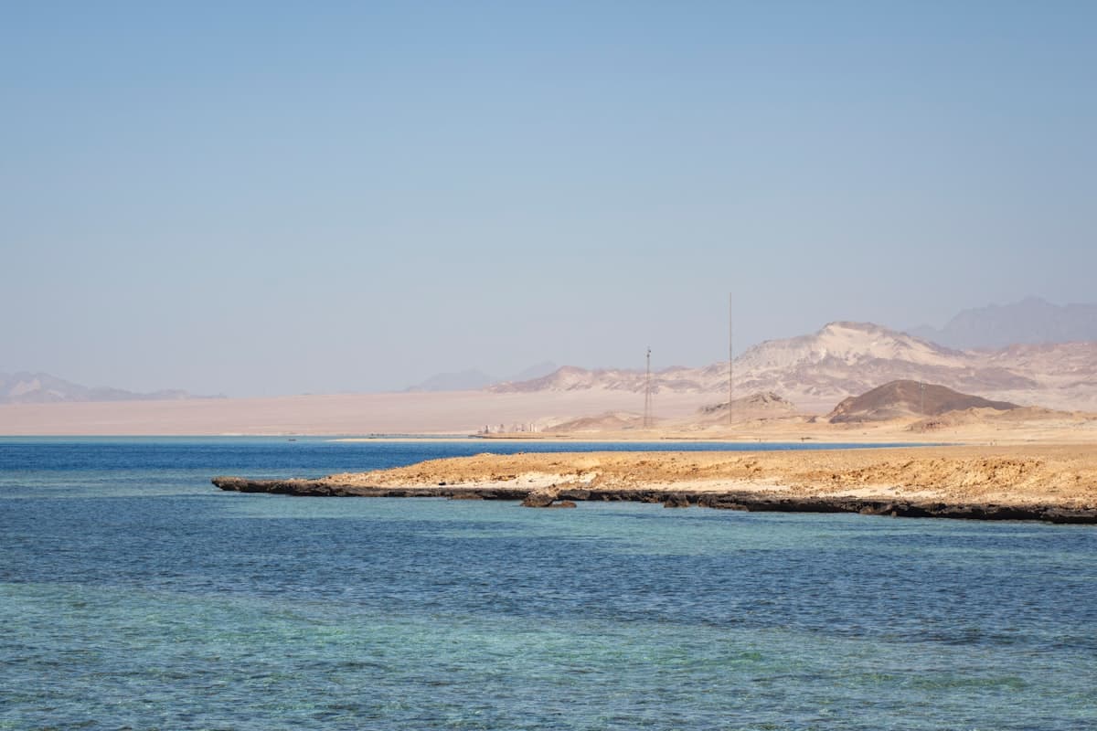 Clear blue water meets a sandy coastline with distant mountains.