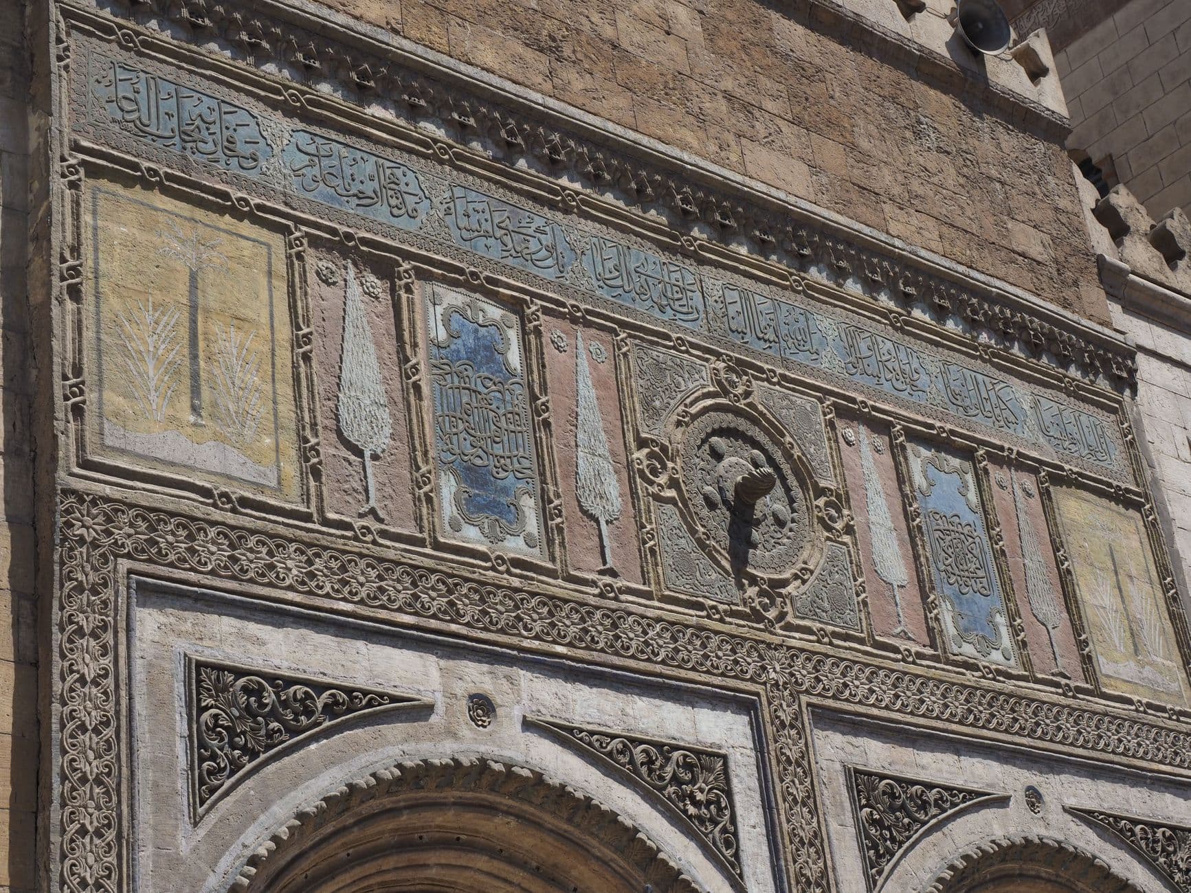 Historic stone facade with detailed Arabic calligraphy and ornamental designs, capturing ancient architectural beauty.