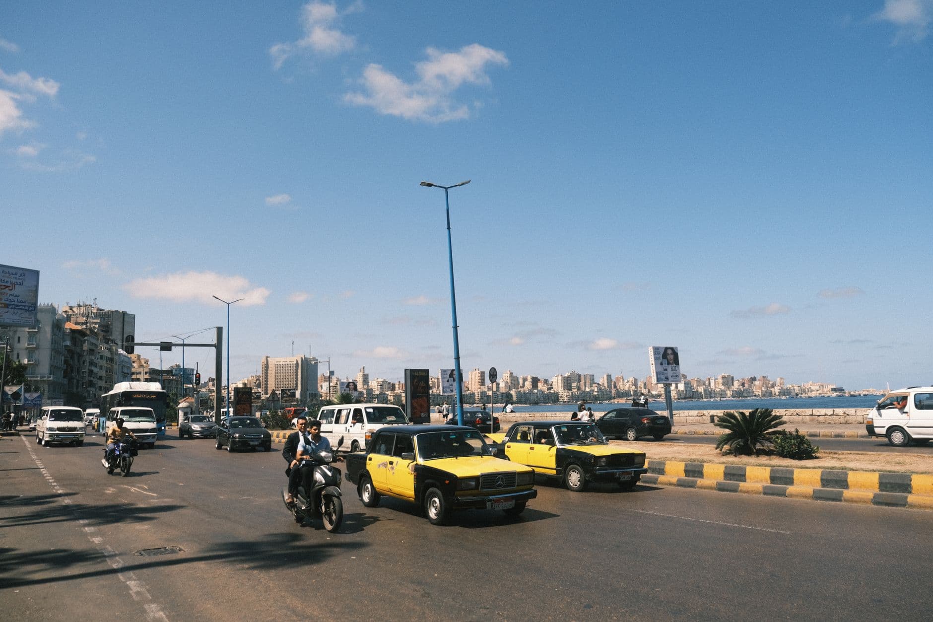 Vibrant street scene in Alexandria, Egypt, featuring yellow taxis and city skyline.