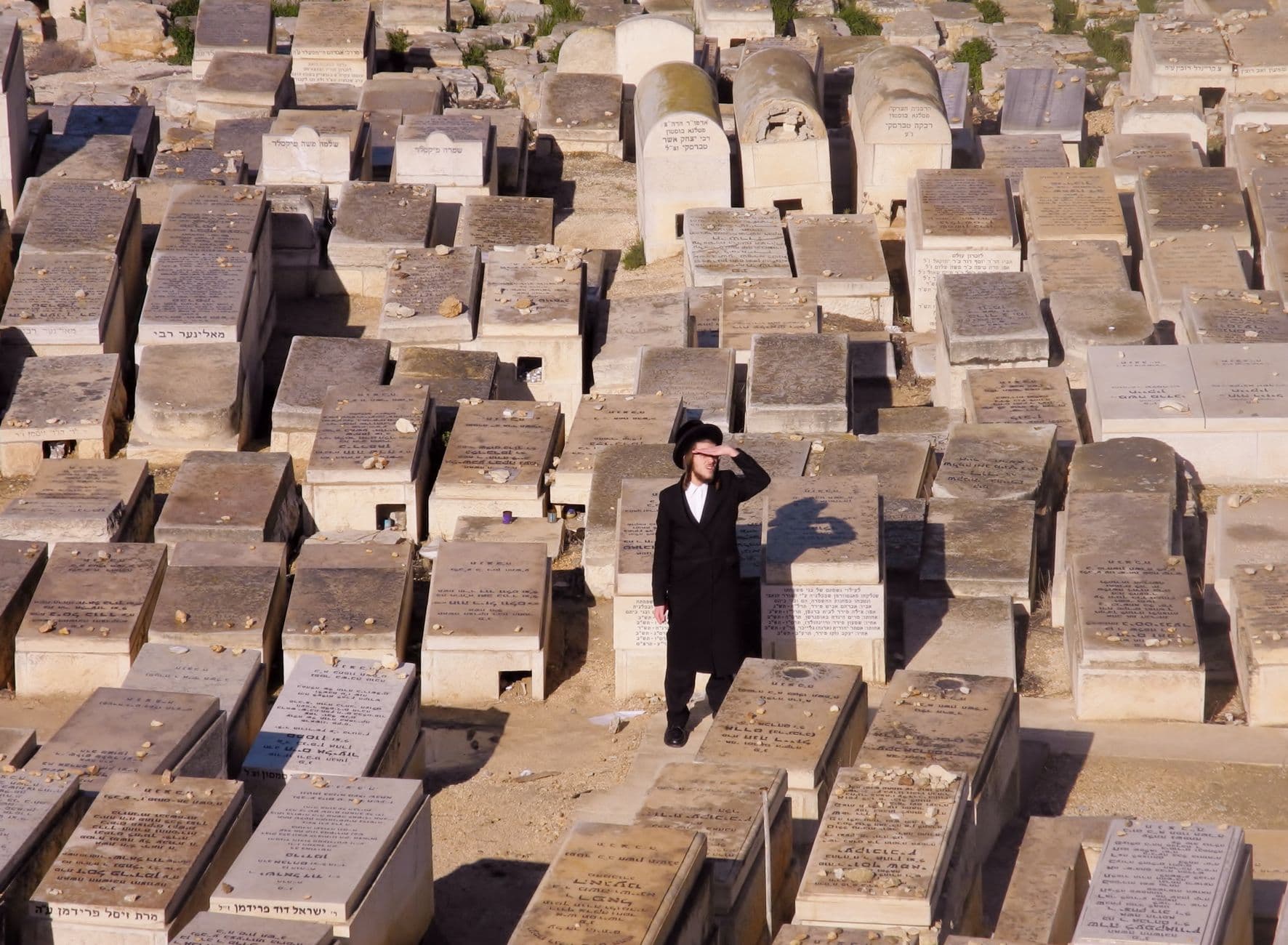 A man stands among gravestones in a Jewish cemetery in Israel on a sunny day.