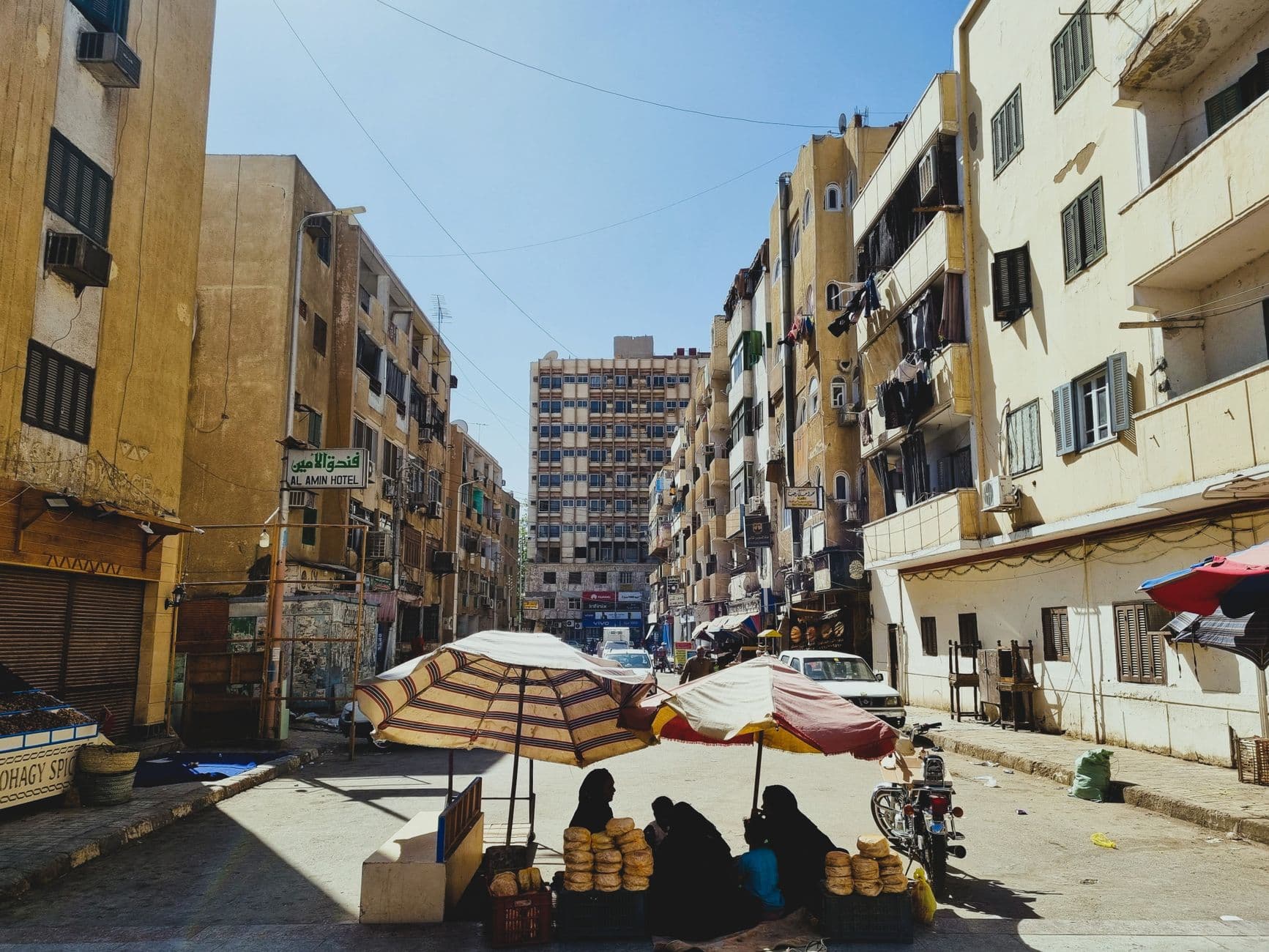 A lively street market with vendors selling bread under colorful umbrellas in an urban setting.