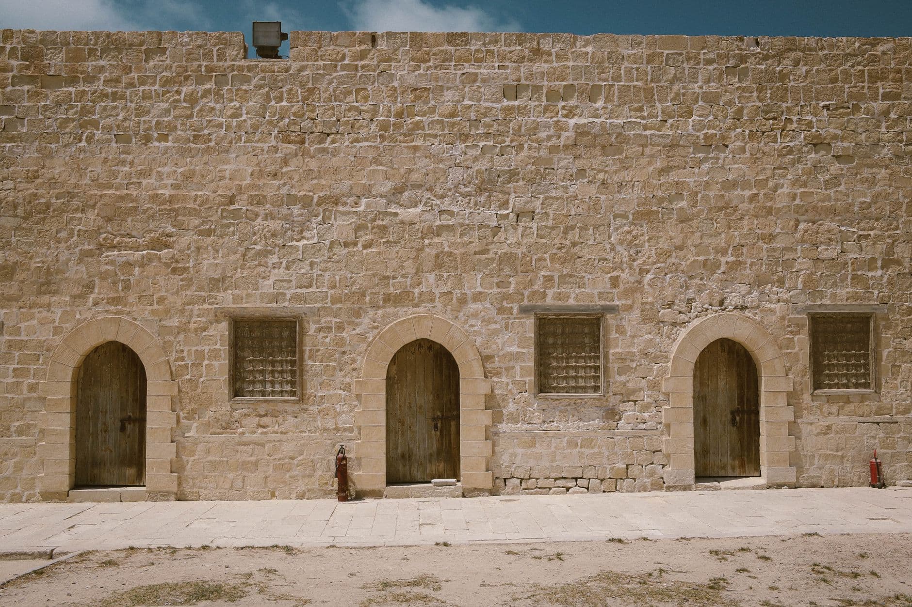 Medieval stone building facade with arched entrances and rustic doors in daylight.