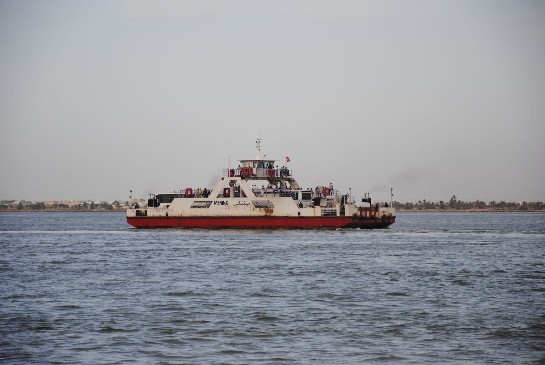A ferry transports passengers across the ocean in Jorf, Tunisia, with a distant coastline in view.