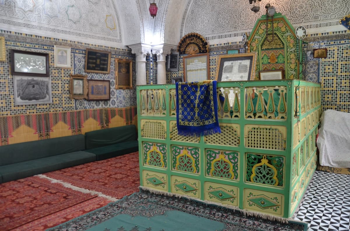 Ornate green tomb enclosure with patterned walls and carpets.