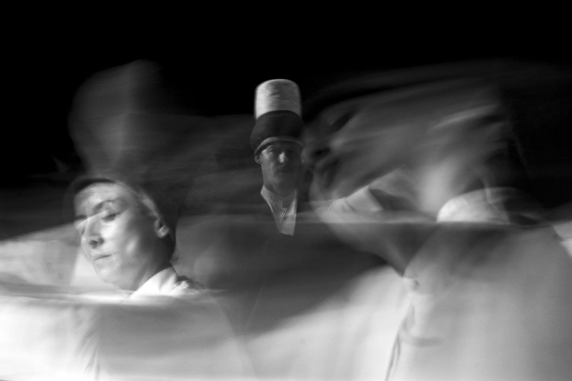 Artistic black and white photo capturing the motion of whirling dervishes performing.