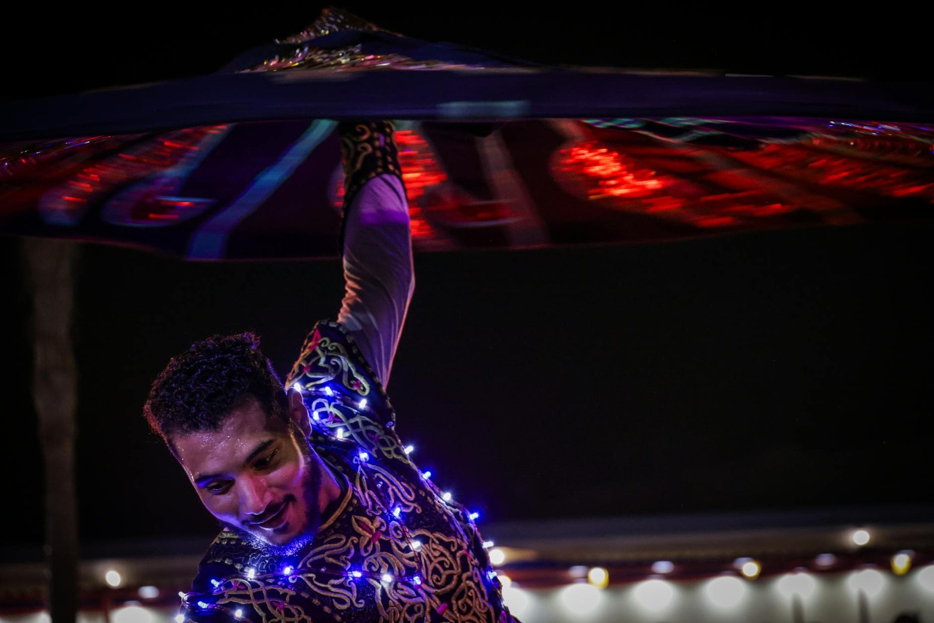 A vibrant Tanoura dancer spinning at night, adorned with lights and colorful costume.