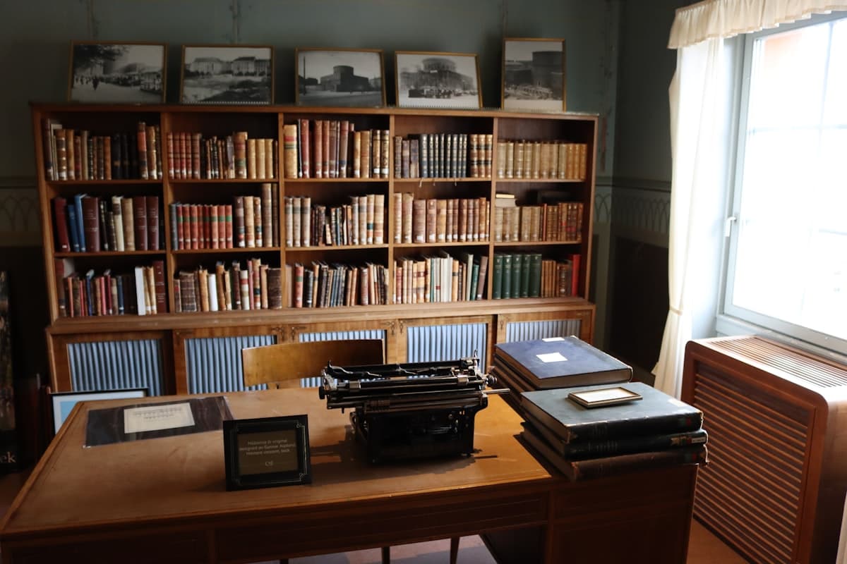 a desk with a typewriter, bookshelf and a window