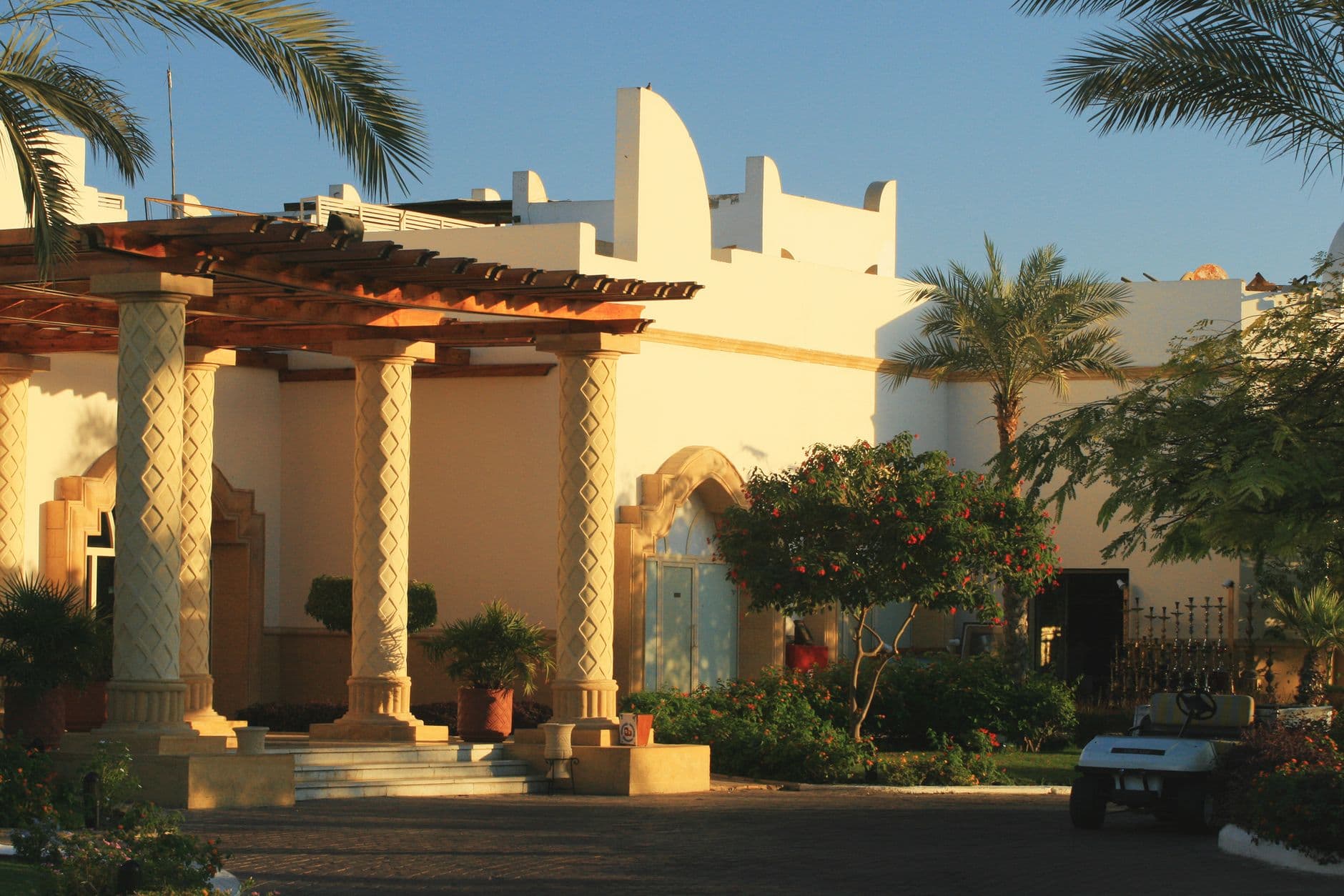 Beautiful Mediterranean style villa entrance with palm trees and pergola at sunset.