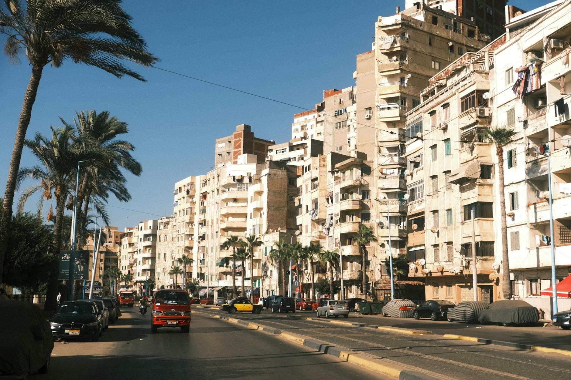 A vibrant street scene in Alexandria, Egypt, showcasing urban life and architecture on a sunny day.