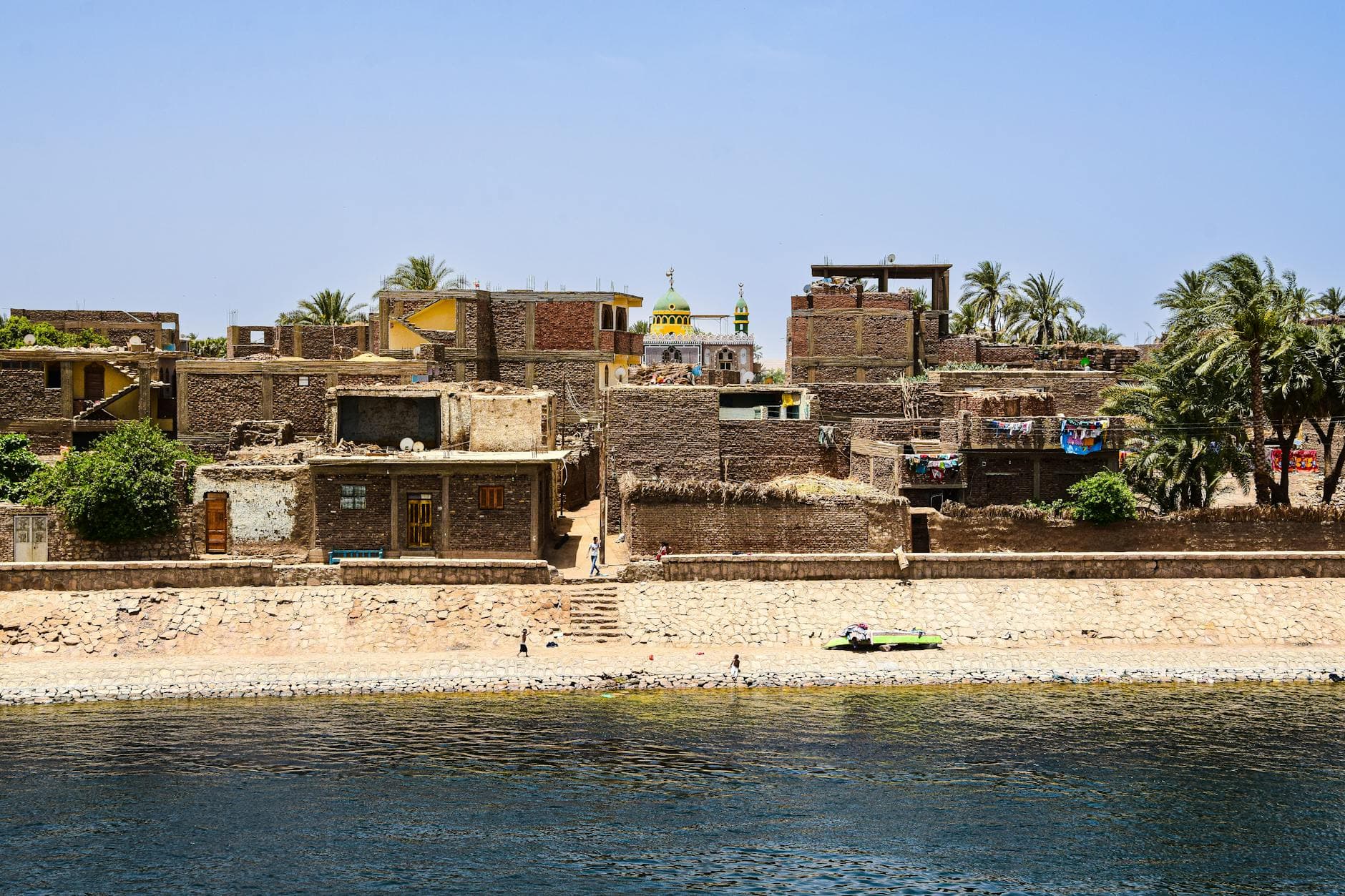 Charming view of a traditional village with historic architecture on the Nile Riverbank under a clear blue sky.